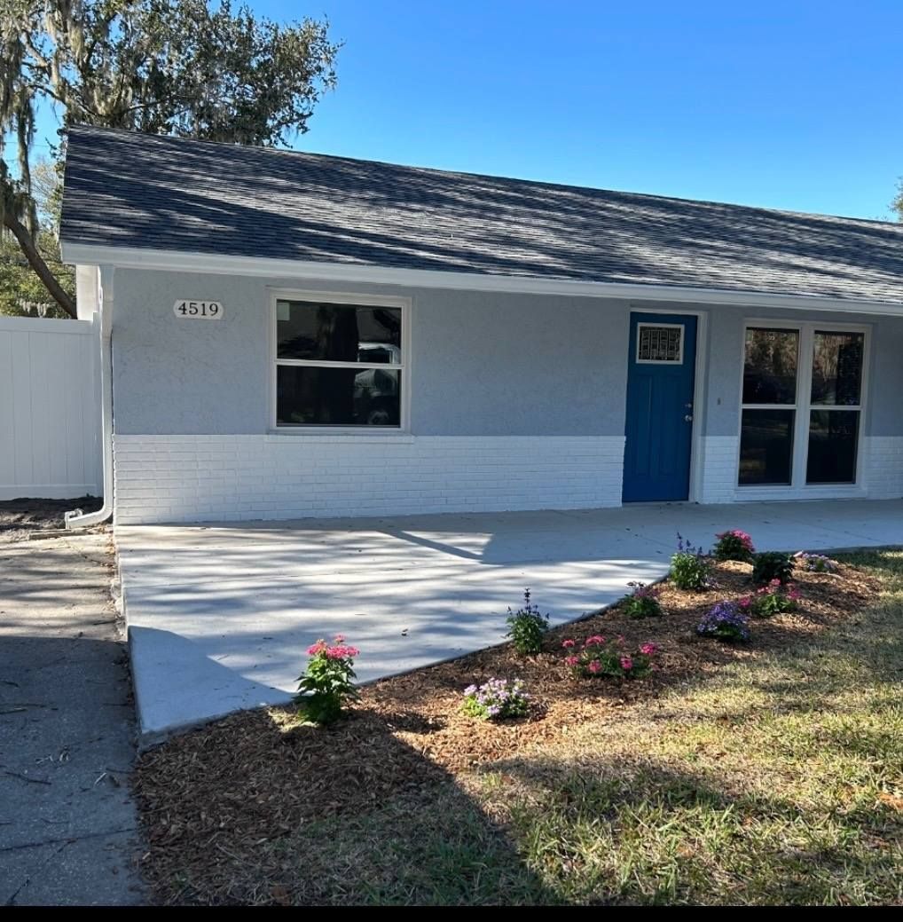 Blue door on a light blue house with white trim and landscaping, set against a blue sky.