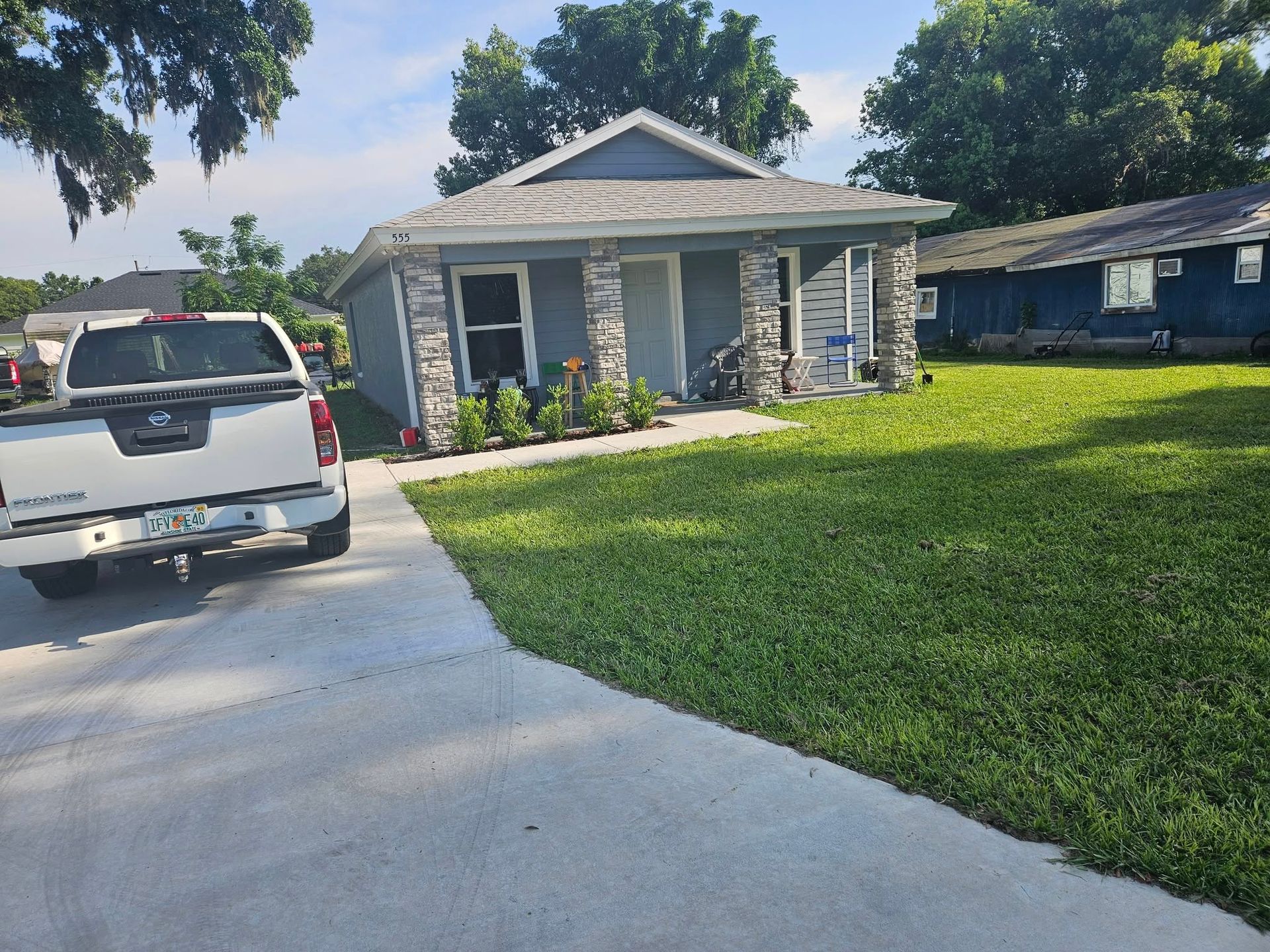 A small house with a white pickup truck parked in the driveway. Green lawn and blue sky.