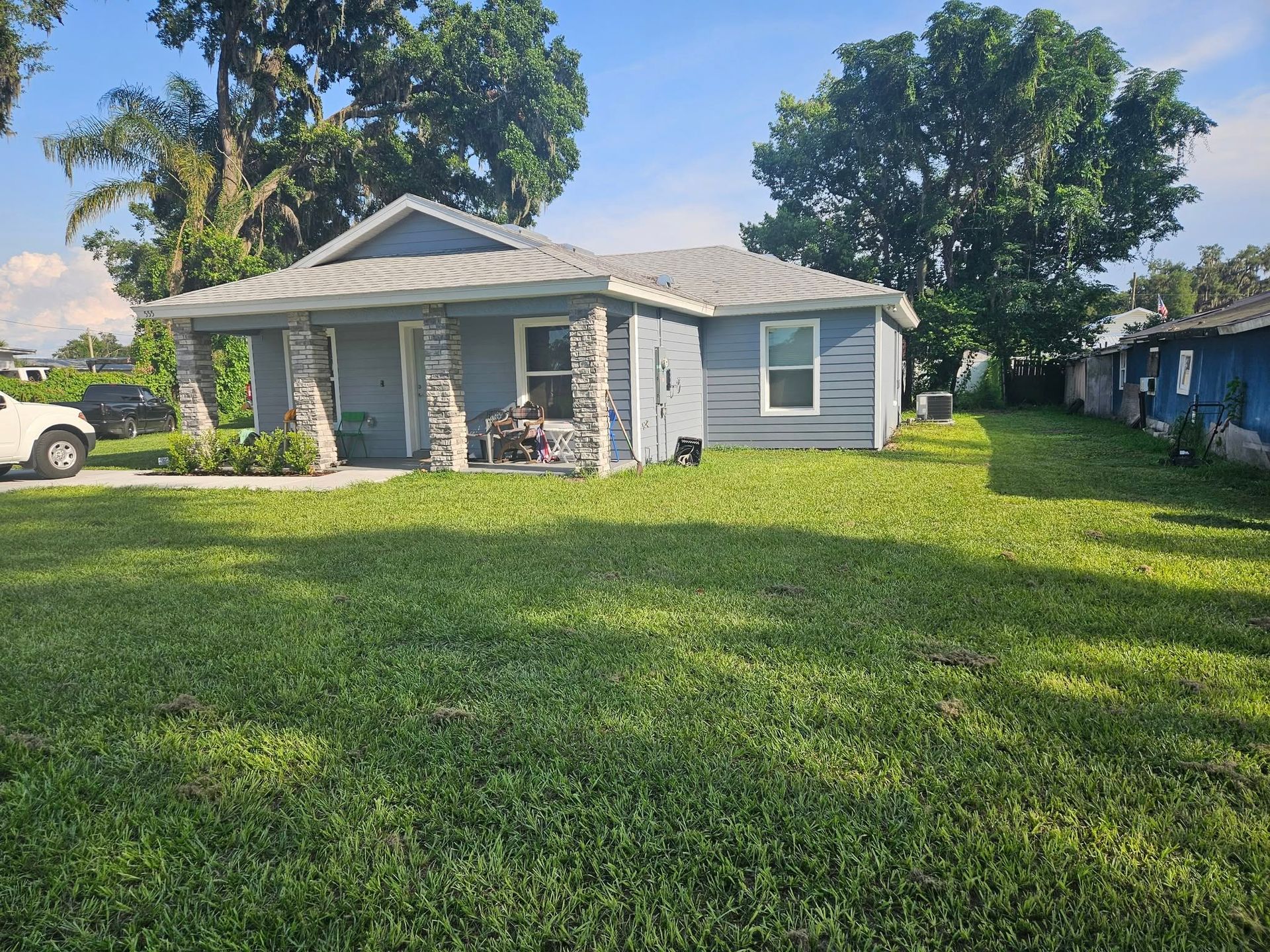 Blue house with stone columns, green lawn, and trees on a sunny day.