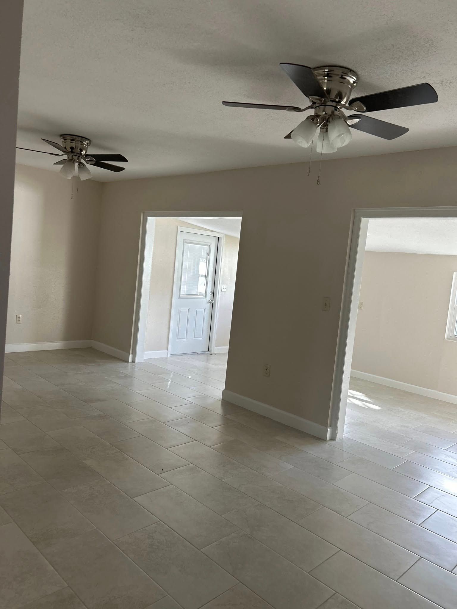 Empty room with tile floors, beige walls, two ceiling fans, doorways leading to other rooms.