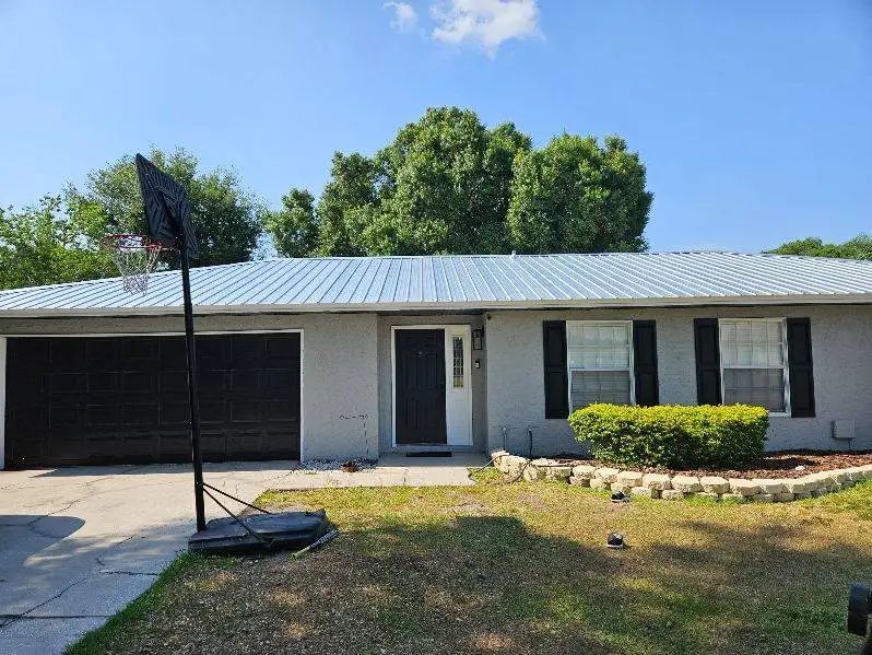 Gray house with metal roof, black garage door, basketball hoop, and green bushes.