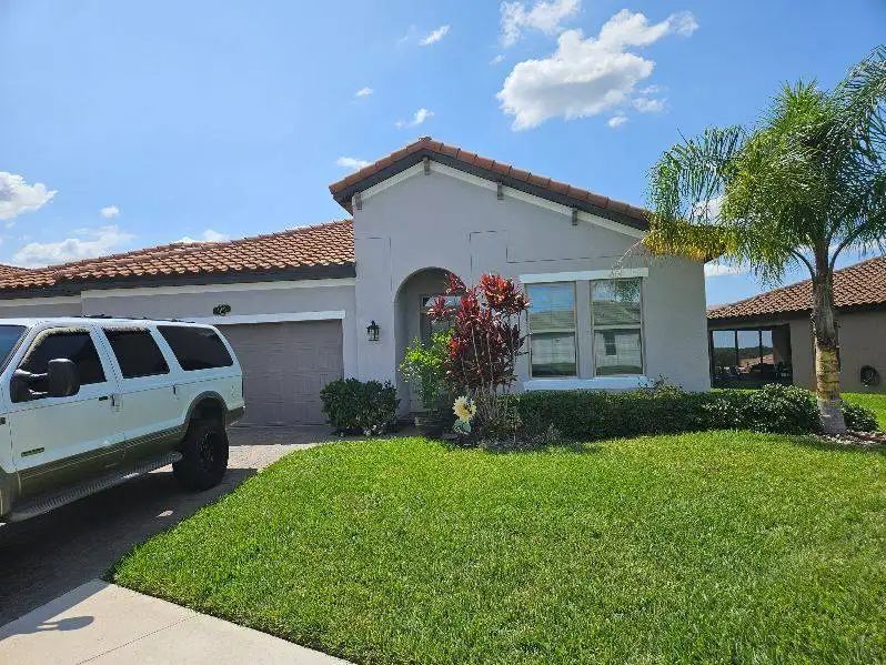 SUV parked in front of a light gray house with red tile roof, green lawn and blue sky.