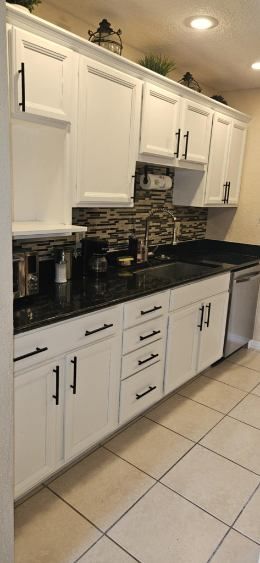 White kitchen cabinets with black countertops, and tile floors.