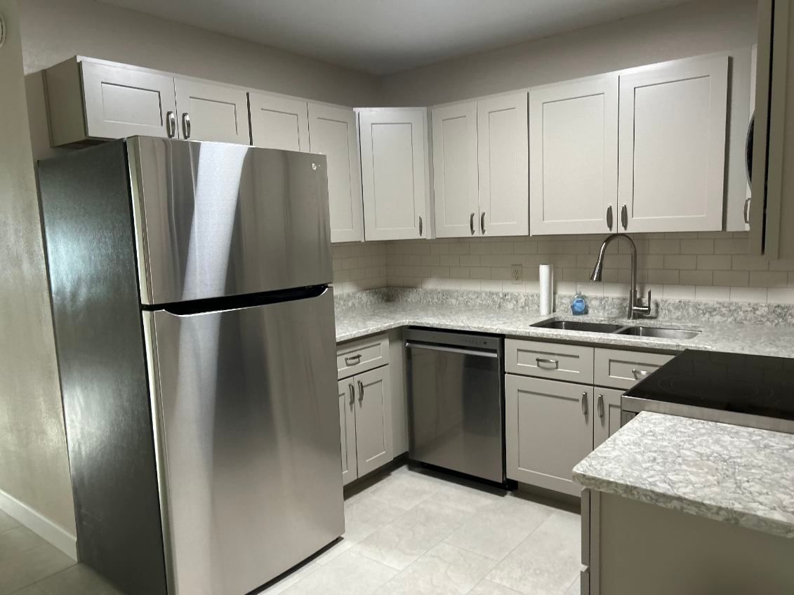 Modern kitchen with stainless steel appliances, light gray cabinets, and speckled countertops.