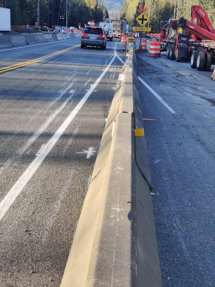 Road construction zone: concrete barriers, lane markings, traffic cones, vehicles.