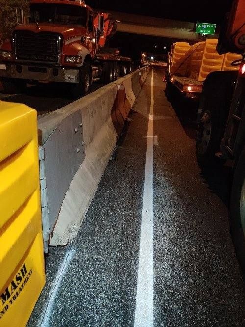 Traffic lane closed by concrete barriers and trucks at night.