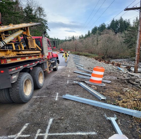 Roadside with work truck, construction debris, and worker. Orange cone. Cloudy day.