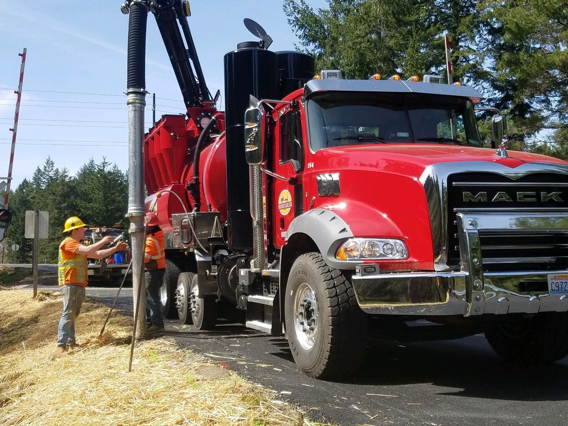 Red Mack truck with workers, vacuuming debris on a road.