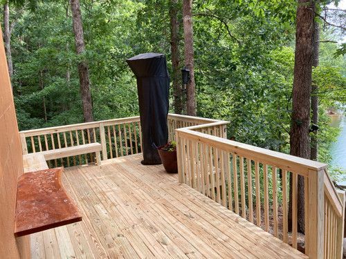 A wooden deck with a grill on it in the middle of a forest.