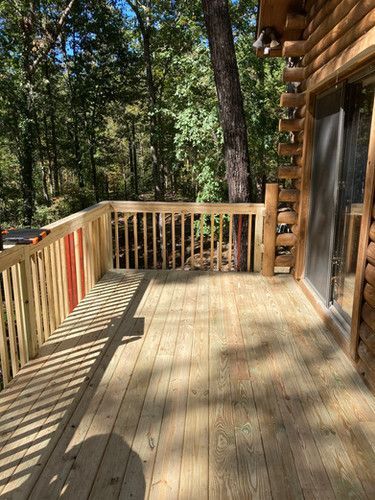A wooden deck with a railing and a sliding glass door on a log cabin.