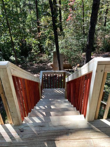 A wooden staircase with a red railing leading up to a wooded area.