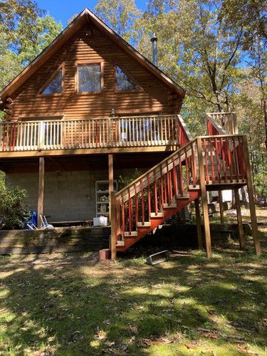 A log cabin with a red deck and stairs in the woods.