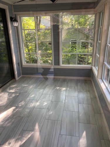 A screened in porch with a lot of windows and tile floors.