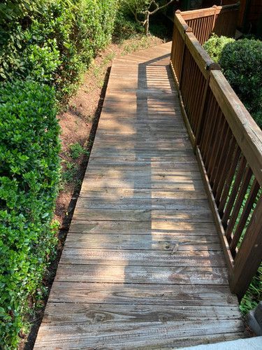 A wooden walkway leading to a deck surrounded by trees and bushes.