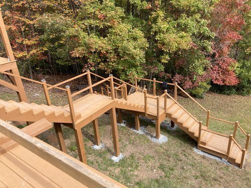 A wooden deck with stairs leading up to it and trees in the background.