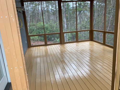 A screened in porch with wooden floors and lots of windows.