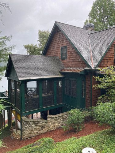 A large brick house with a green porch overlooking a lake.