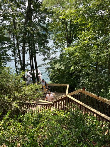 A man is sitting on a wooden deck overlooking a lake surrounded by trees.