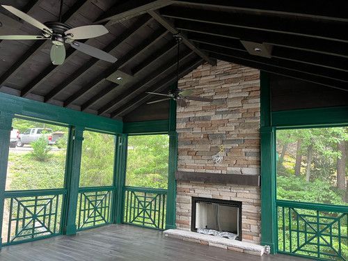 A screened in porch with a fireplace and a ceiling fan