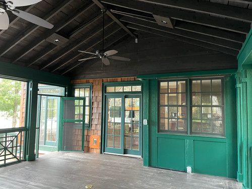 There is a porch with a ceiling fan and a lot of windows.