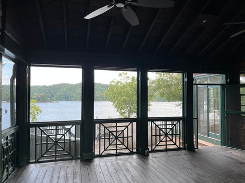 A screened in porch with a ceiling fan and a view of a lake.