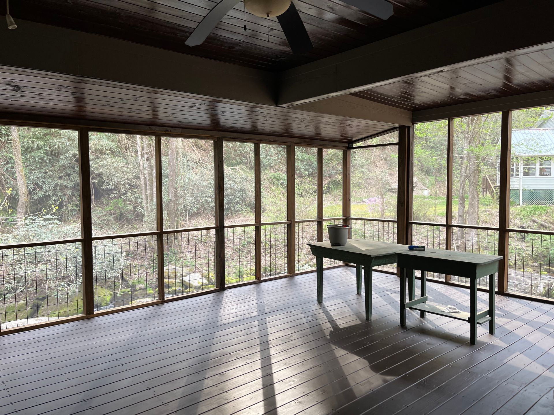 A screened in porch with a table and a ceiling fan.