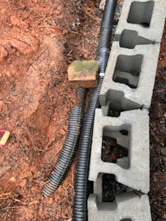 A hose is sitting next to a brick block in the dirt.