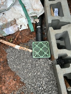 A green drain box is sitting on top of a pile of gravel next to a drain pipe.