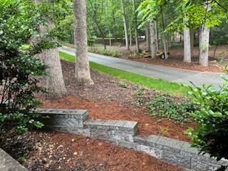 A stone wall with steps leading up to a road surrounded by trees.