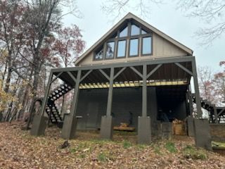 A house with a large deck and stairs is surrounded by trees.