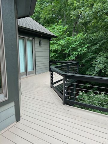 A wooden deck with a black railing is next to a house.