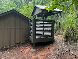 A wooden shed is sitting in the middle of a forest next to a fence.
