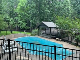 A large swimming pool with a gazebo in the backyard surrounded by trees.