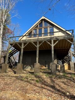 A house with a large deck is sitting on top of a hill in the woods.