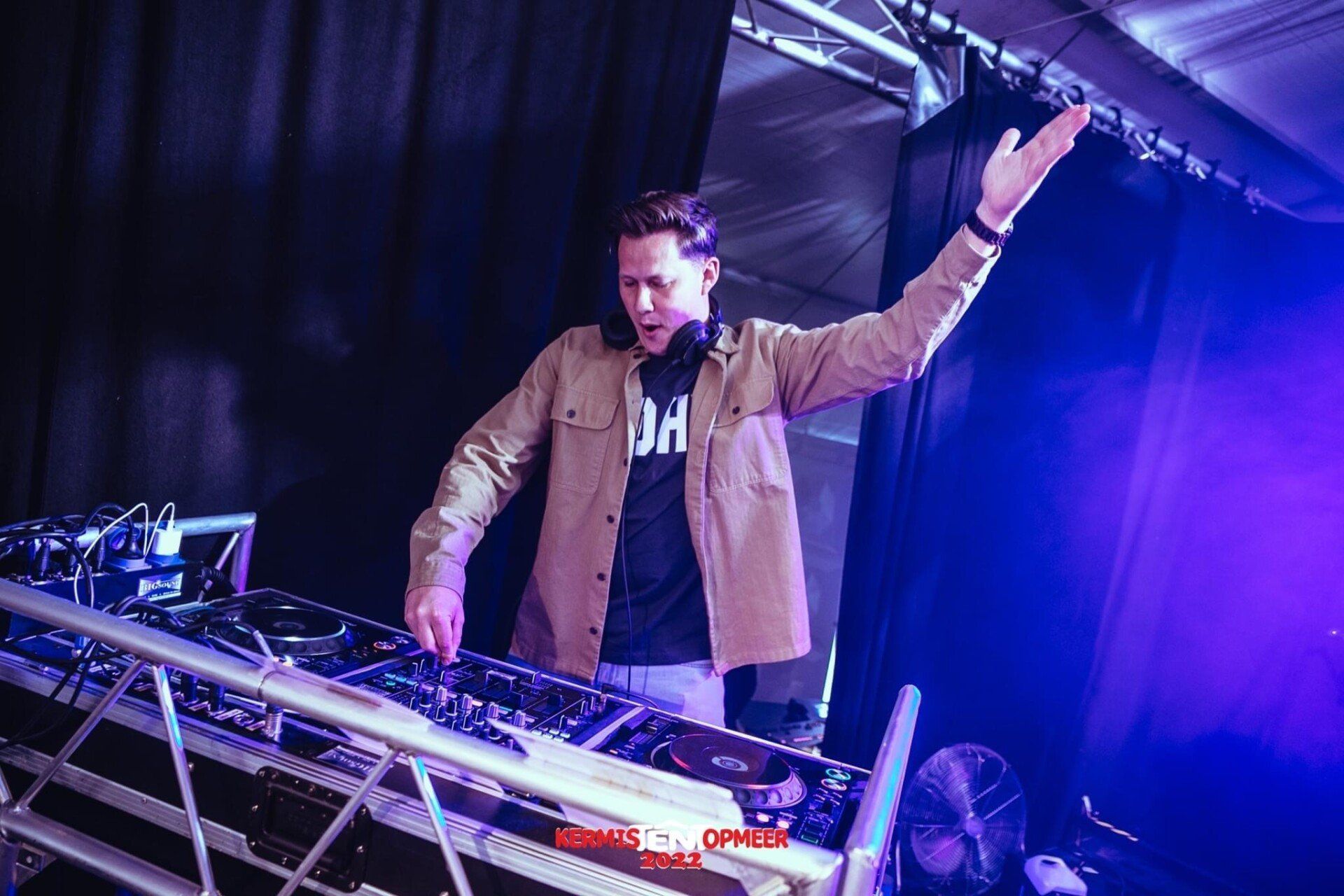 Een man draait een dj-set op een podium met zijn hand in de lucht.
