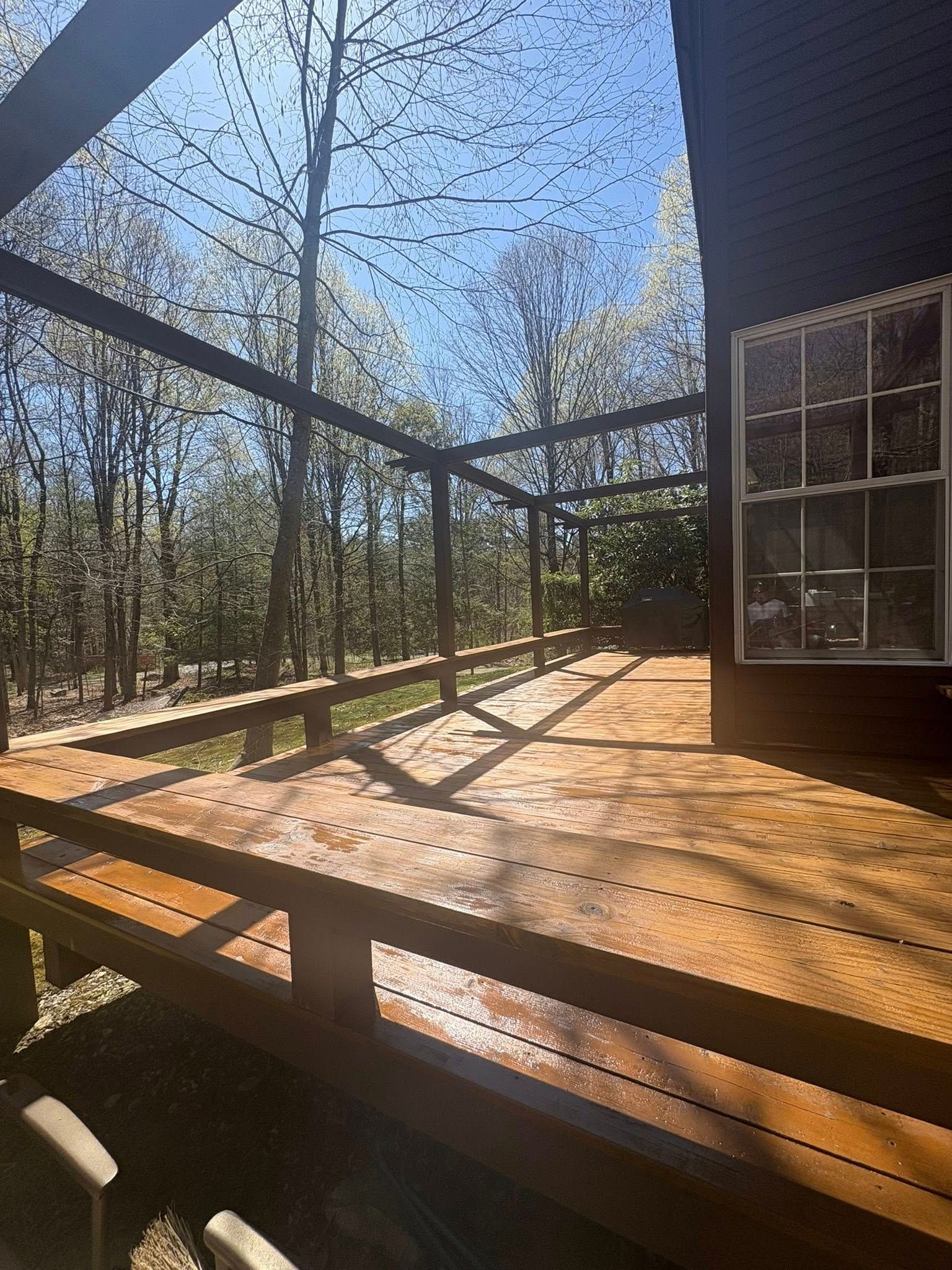 A large, wooden deck with a built-in bench railing, attached to the side of a dark house overlooking a wooded area.