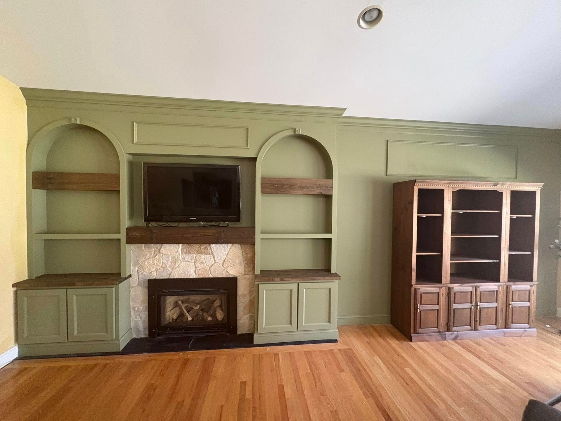 A living room features green built-in shelves and fireplace with a wall-mounted TV, plus a matching wooden bookcase.