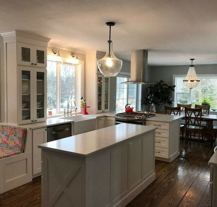 A white farmhouse-style kitchen with a central island, glass-front cabinets, pendant lights, and dark wood flooring.