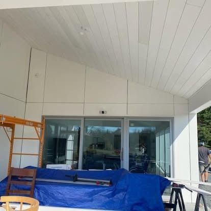 A construction site with a white, sloped ceiling and sliding glass doors, featuring a blue-covered workbench.