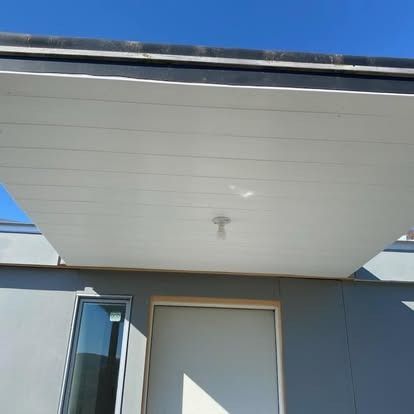 A white porch ceiling overhangs a doorway and window on a gray building under a clear blue sky.