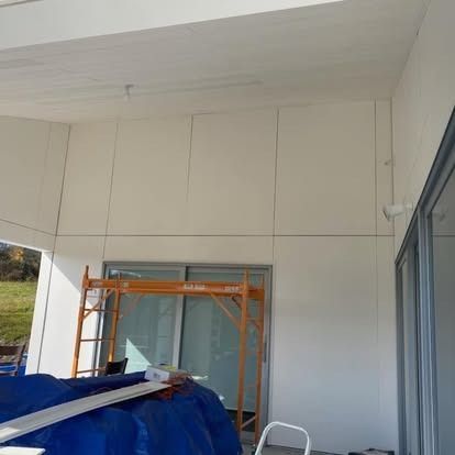 A construction scaffold stands in front of a white wall under a partially completed ceiling on a house patio.