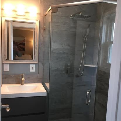 Modern bathroom with a white vanity sink, a square mirror, and a glass-enclosed shower featuring dark gray tiled walls.
