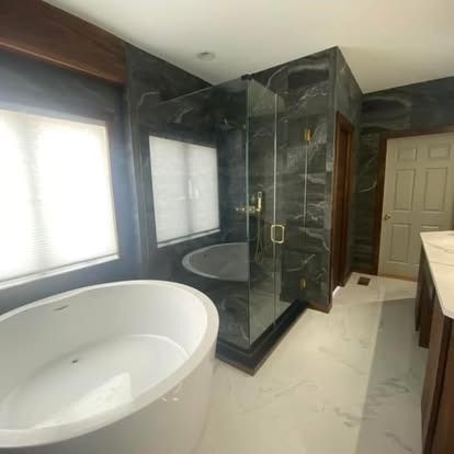 Modern bathroom featuring a white freestanding tub, a glass-enclosed shower with dark marble tiles, and white floor tiles.