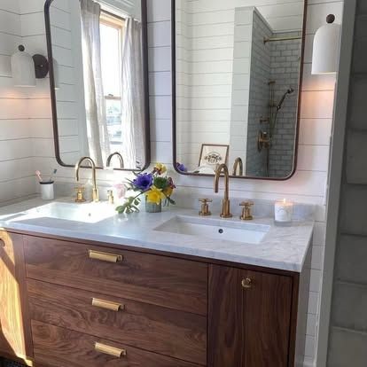 A modern bathroom vanity with a wood cabinet, white countertop, dual mirrors, and gold fixtures against white shiplap.