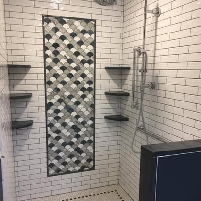 A modern tiled shower with white subway walls, a black-and-white scallop tile accent stripe, and corner shelves.