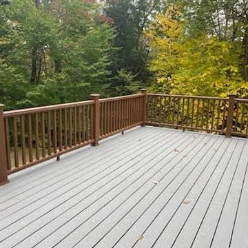 A raised, gray composite deck with brown wooden railings, surrounded by autumn trees.