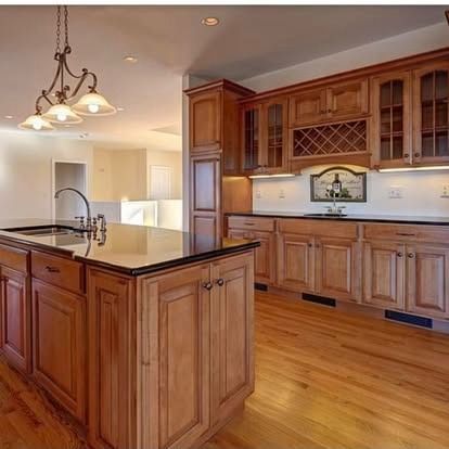 A spacious kitchen with natural wood cabinets, black countertops, a central island, and a three-light pendant fixture.