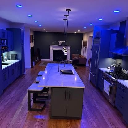 A modern kitchen with dark blue cabinetry, a long marble-topped island, and overhead pendant lights in a dimly lit space.