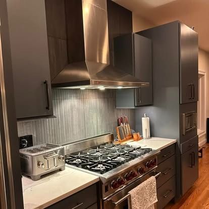 A modern kitchen featuring charcoal cabinets, a stainless steel range hood, a gas stovetop, and a toaster on the counter.