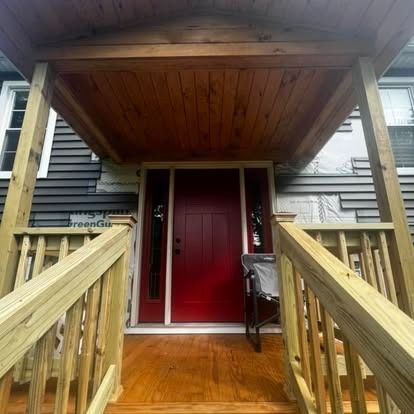 A wooden porch with railings leads to a bright red front door, with dark gray siding visible on the exterior walls.